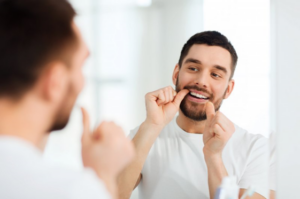 Man flossing his teeth in mirror after removing Invisalign 